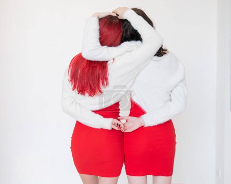 Photo for Rear view of two women dressed in identical red dresses and white sweaters. Lesbian intimacy. White background - Royalty Free Image