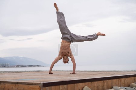 Photo for Shirtless caucasian man doing acrobatic wheel on the beach - Royalty Free Image