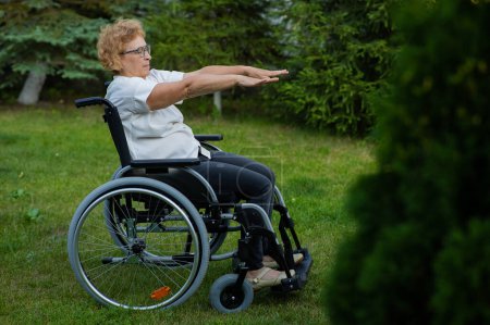Téléchargez les photos : Femme caucasienne âgée faisant des exercices assis dans un fauteuil roulant à l'extérieur - en image libre de droit