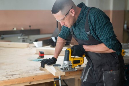 Téléchargez les photos : Un homme coupe une planche de bois avec un puzzle électrique dans un atelier - en image libre de droit