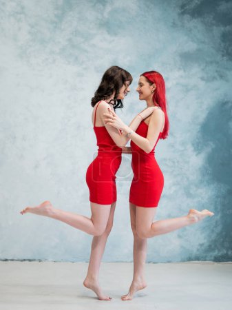 Photo for Full-length portrait of two tenderly embracing women dressed in identical red dresses. Lesbian intimacy - Royalty Free Image