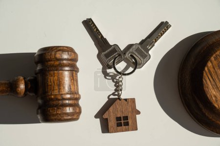 Keys with a keychain in the shape of a house and a judges gavel on a white background