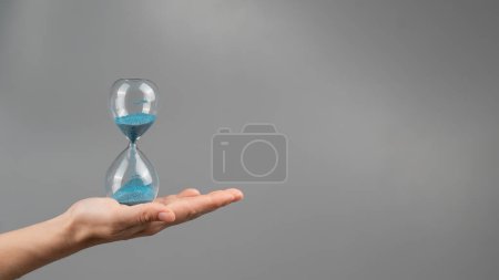 Foto de Mujer sosteniendo un reloj de arena sobre un fondo gris. Primer plano. Copiar espacio - Imagen libre de derechos