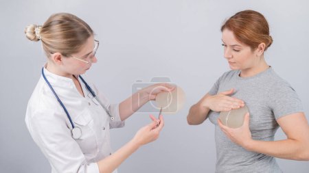 Mujer caucásica probándose implantes mamarios. Un cirujano plástico ayuda a un paciente con una elección