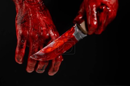 Téléchargez les photos : Homme tenant un couteau avec une main sanglante sur fond noir - en image libre de droit