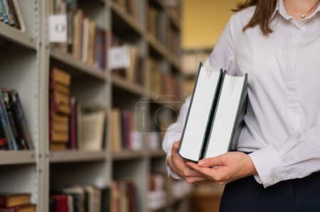 Téléchargez les photos : Gros plan des mains féminines avec des livres dans la bibliothèque publique - en image libre de droit