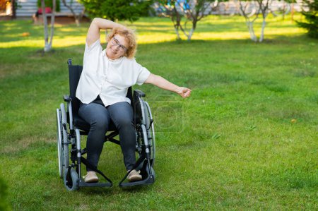 Photo for Elderly caucasian woman doing exercises while sitting in a wheelchair outdoors - Royalty Free Image