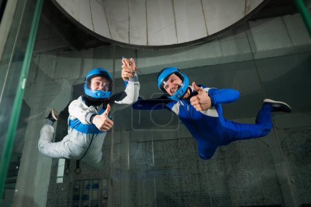 Photo for A man and a woman enjoy a joint flight in a wind tunnel and give a thumbs up. Free fall simulator - Royalty Free Image
