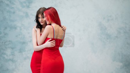Photo for A close-up portrait of two tenderly embracing women dressed in identical red dresses. Lesbian intimacy - Royalty Free Image