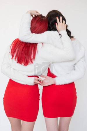Photo for Rear view of two women dressed in identical red dresses and white sweaters. Lesbian intimacy. White background - Royalty Free Image