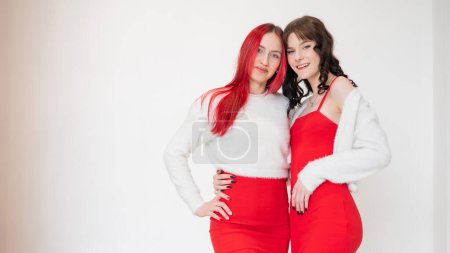 Photo for Two women dressed in identical red dresses and white sweaters. Lesbian intimacy. White background - Royalty Free Image