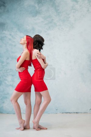 Photo for A full-length portrait of two women dressed in identical red dresses and standing back to back. Lesbian intimacy - Royalty Free Image