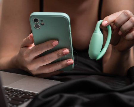 A woman lies on a bed and synchronizes the kegel machine with a smartphone