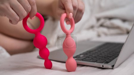 Photo for Woman holding a set of anal beads next to a laptop while lying in bed - Royalty Free Image