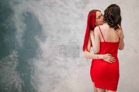Photo for A close-up portrait of two tenderly embracing women dressed in identical red dresses. Lesbian intimacy - Royalty Free Image