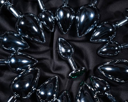 Foto de Muchos tapones anales de metal en una sábana de seda negra - Imagen libre de derechos
