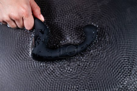 Photo for A woman holds a black prostate stimulator that vibrates and creates ripples on the surface of the water against a black background - Royalty Free Image
