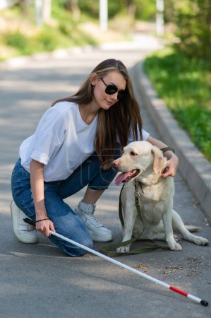 Photo for Blind young woman cuddling with guide dog on a walk outdoors - Royalty Free Image