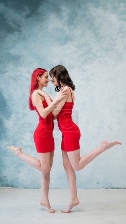 Photo for Full-length portrait of two tenderly embracing women dressed in identical red dresses. Lesbian intimacy - Royalty Free Image