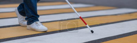 Photo for Close-up of the legs of a blind woman crossing the road at a crosswalk with a cane. Widescreen - Royalty Free Image