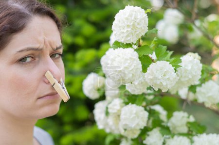 Téléchargez les photos : Unhappy woman with a clothespin on her nose on a walk in a blooming park - en image libre de droit