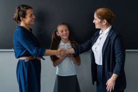 Photo for The teacher shakes hands with the mother of the schoolgirl standing at the blackboard - Royalty Free Image
