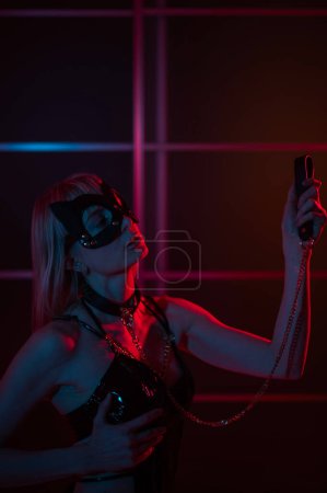 Foto de Chica rubia en una máscara de cuero y esposas en el dormitorio en luz de neón azul rojo. Juegos de rol - Imagen libre de derechos
