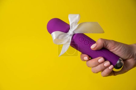 Woman holding purple vibrator with white bow on yellow background. Copy space