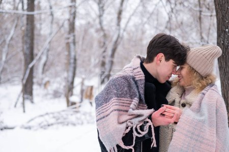 Foto de Una joven pareja camina en el parque en invierno. El chico y la chica están bebiendo una bebida caliente al aire libre - Imagen libre de derechos