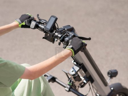 Foto de Una mujer controla una silla de ruedas usando un dispositivo manual especial. Primer plano de las manos femeninas en la bicicleta eléctrica - Imagen libre de derechos