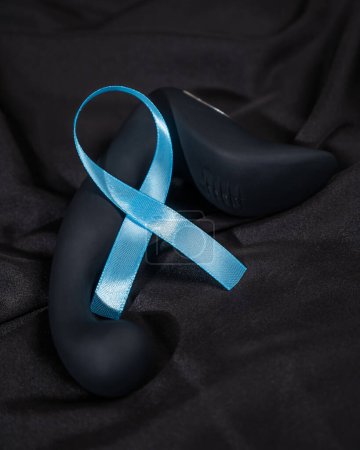 Téléchargez les photos : Stimulateur de prostate et ruban bleu sur une feuille de soie noire. Symbole de lutte contre le cancer de la prostate - en image libre de droit