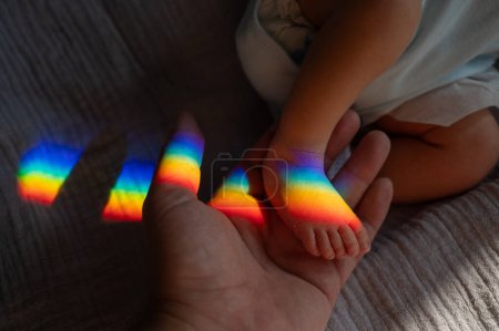 Photo for A man holds his newborn son by the leg. Beam of light through a prism - Royalty Free Image
