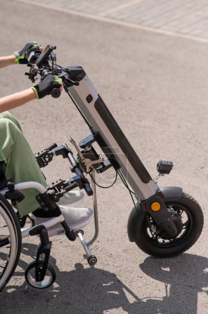 Foto de Una mujer controla una silla de ruedas usando un dispositivo manual especial. Cerrar una bicicleta eléctrica - Imagen libre de derechos