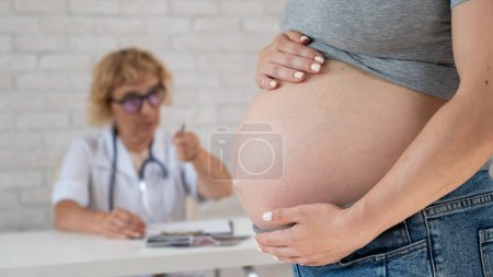 Photo for Doctor obstetrician gynecologist at his desk in the background. Close-up of a pregnant womans belly - Royalty Free Image