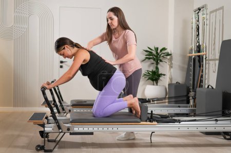 Photo for A pregnant woman works out on a reformer exercise machine with a personal trainer - Royalty Free Image