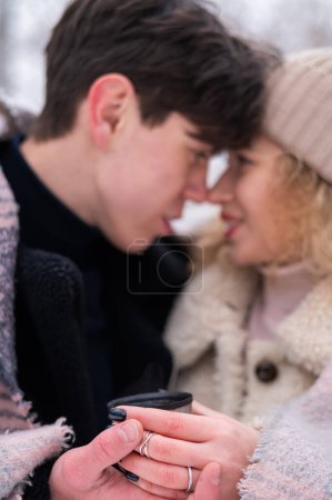 Foto de Una joven pareja camina en el parque en invierno. El chico y la chica están bebiendo una bebida caliente al aire libre - Imagen libre de derechos