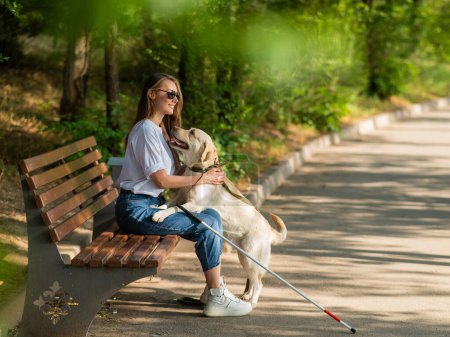 Photo for Blind young woman cuddling with guide dog while sitting on a bench - Royalty Free Image