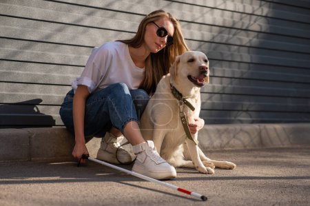 Photo for A blind woman walks her guide dog on the street. Girl hugging a labrador - Royalty Free Image