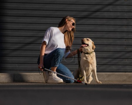 Photo for A blind woman walks her guide dog on the street. Girl hugging a labrador - Royalty Free Image