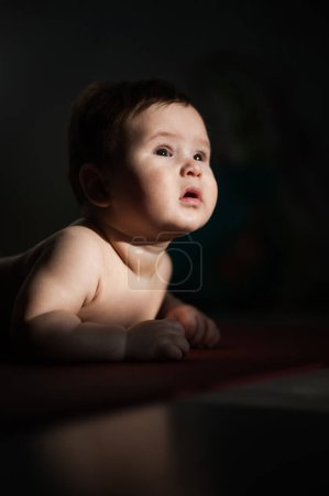 Photo for A cute little boy lies on his forearms on the floor. Vertical photo - Royalty Free Image