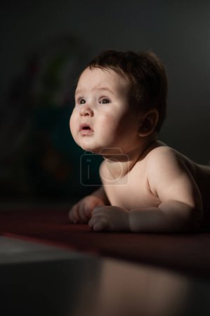A cute little boy lies on his forearms on the floor. Vertical photo
