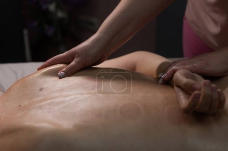 Frau bei einer therapeutischen Rückenmassage. Der Masseur knetet die Muskeln unter dem Schulterblatt