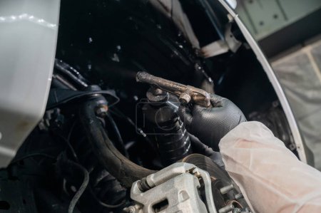 Ein Automechaniker trägt Korrosionsschutzmastix auf den Unterboden eines Autos auf