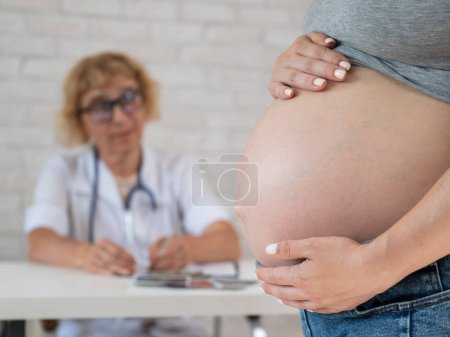 Photo for Doctor obstetrician gynecologist at his desk in the background. Close-up of a pregnant womans belly - Royalty Free Image