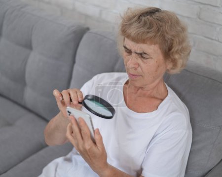 Ältere kaukasische Frau mit Kurzsichtigkeit beim Versuch, eine Nachricht mit einer Lupe auf einem Smartphone zu lesen