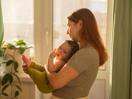 Kaukasierin hält ihren neugeborenen Sohn zärtlich am Fenster