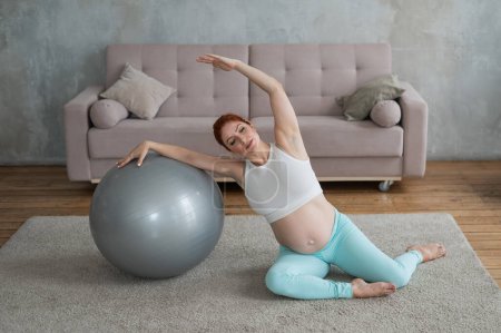 Photo for Pregnant woman doing side bends with a fitness ball at home - Royalty Free Image
