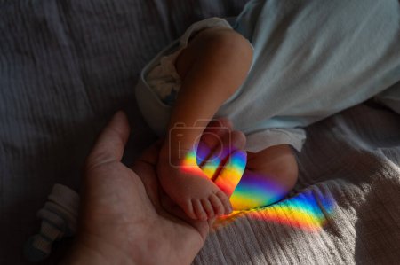 Ein Mann hält seinen neugeborenen Sohn am Bein. Lichtstrahl durch ein Prisma