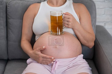 A faceless pregnant woman sits on the sofa and holds a glass of beer on her stomach. Skin rash