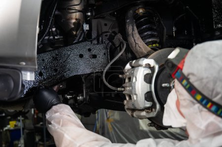 Ein Automechaniker trägt Korrosionsschutzmastix auf den Unterboden eines Autos auf